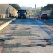 A bridge with construction pavement markings, cones, and a construction vehicle in the background