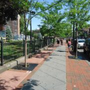 A sidewalk with trees and vehicles parked on the road.
