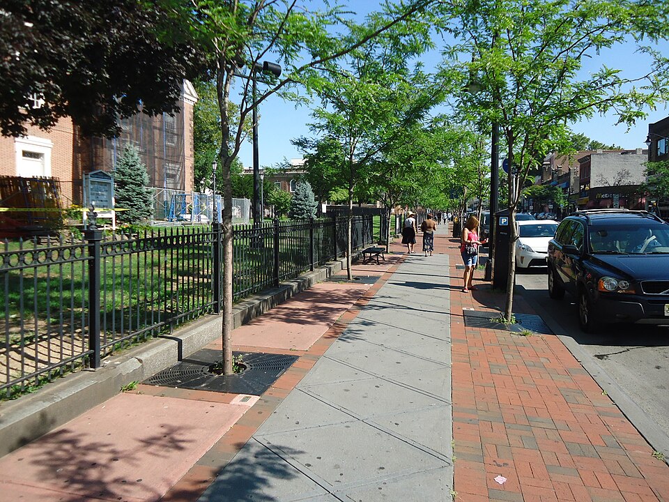 A sidewalk with trees and vehicles parked on the road.